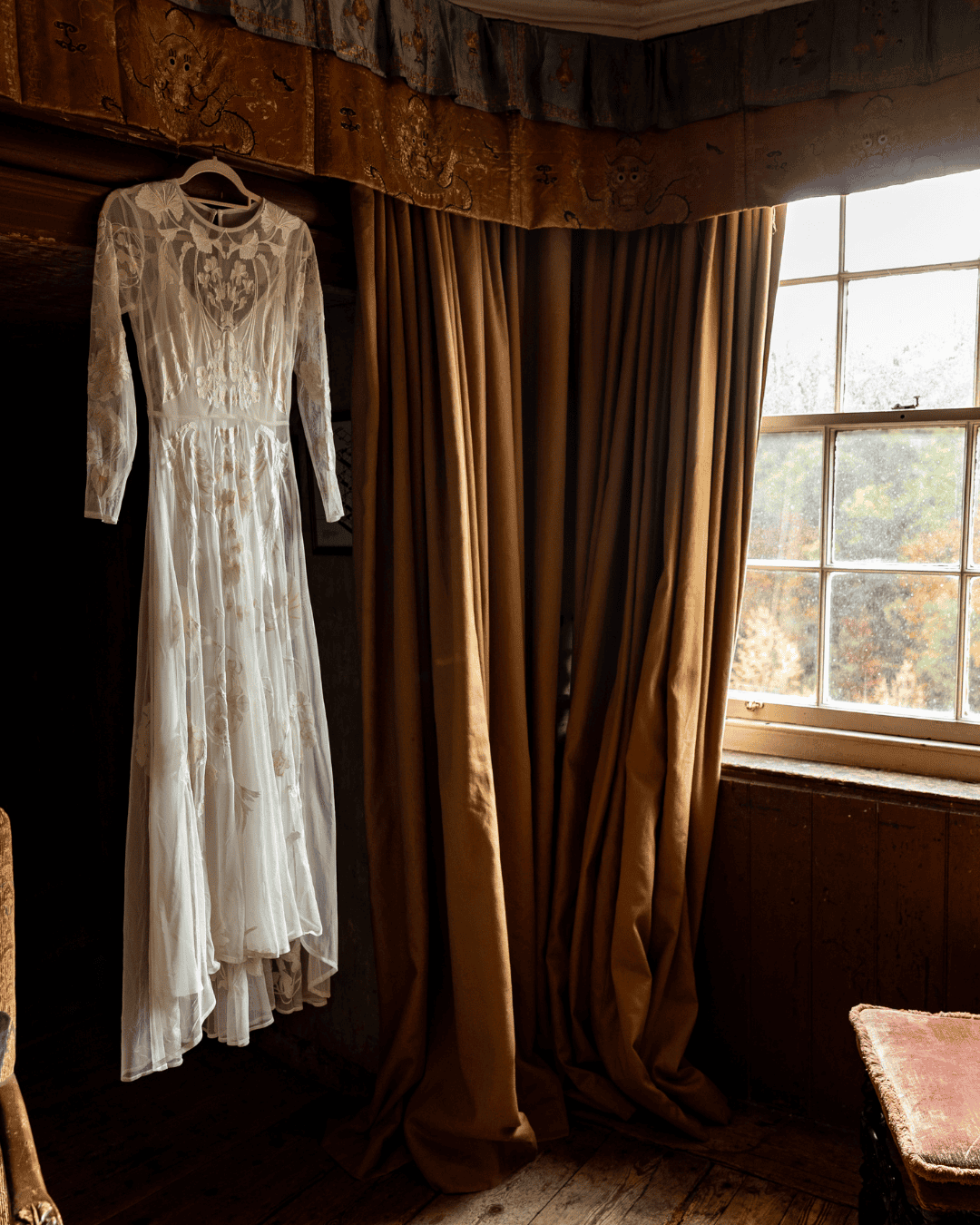 Bride's lace wedding dress hanging in a warmly-lit room