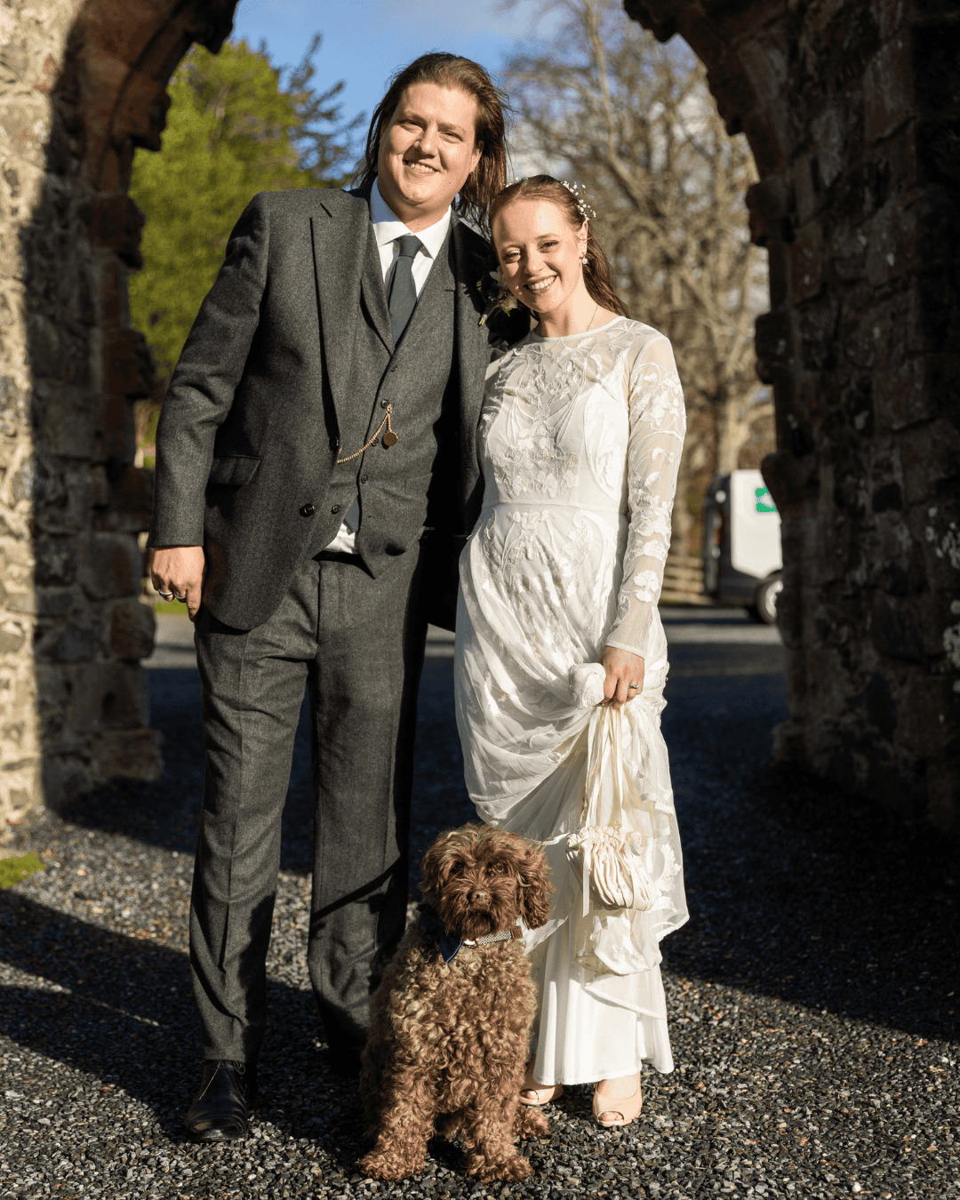 Bride and groom with their dog under a stone arch