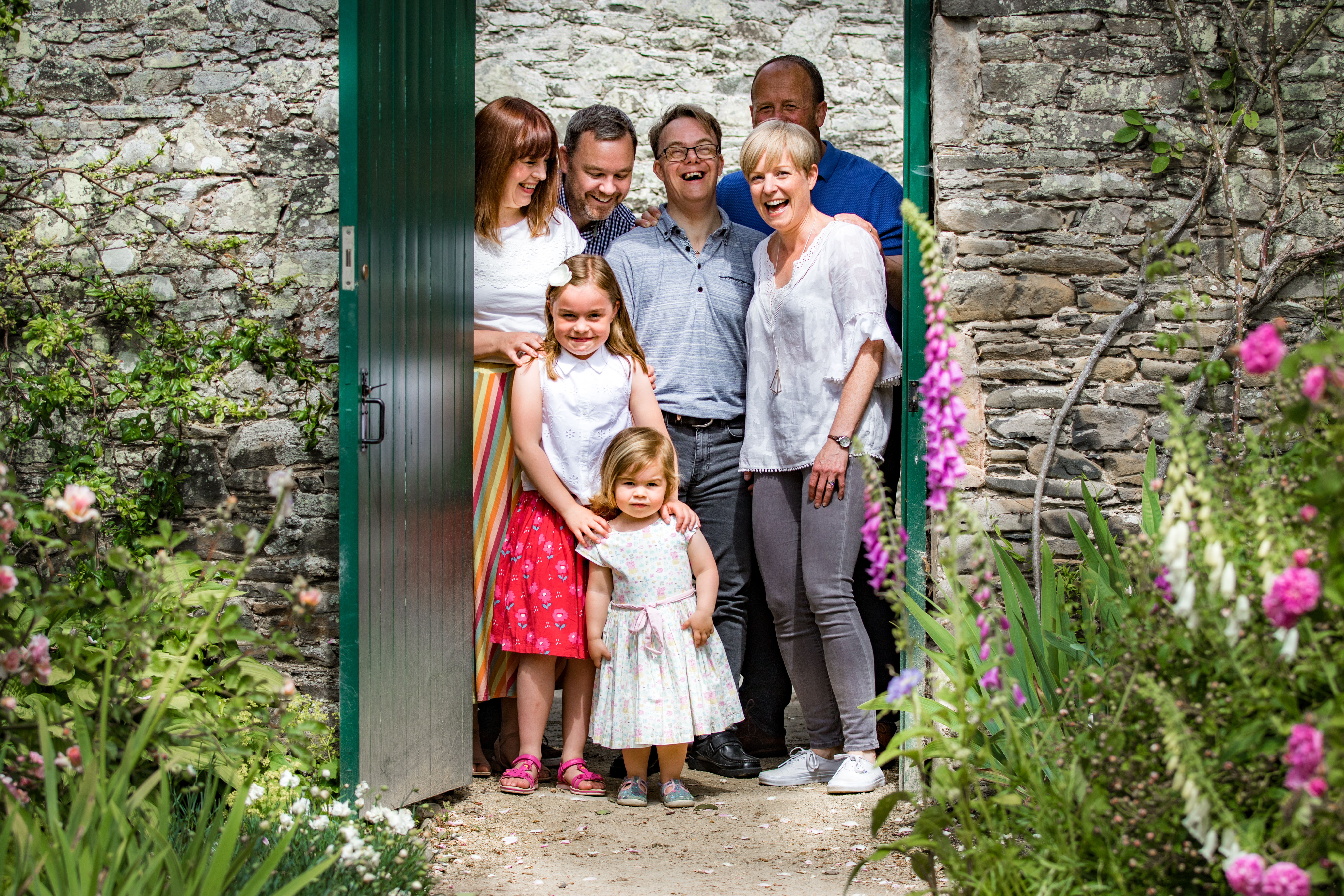 Family gathered smiling in a green garden doorway framed by foxgloves and stone walls