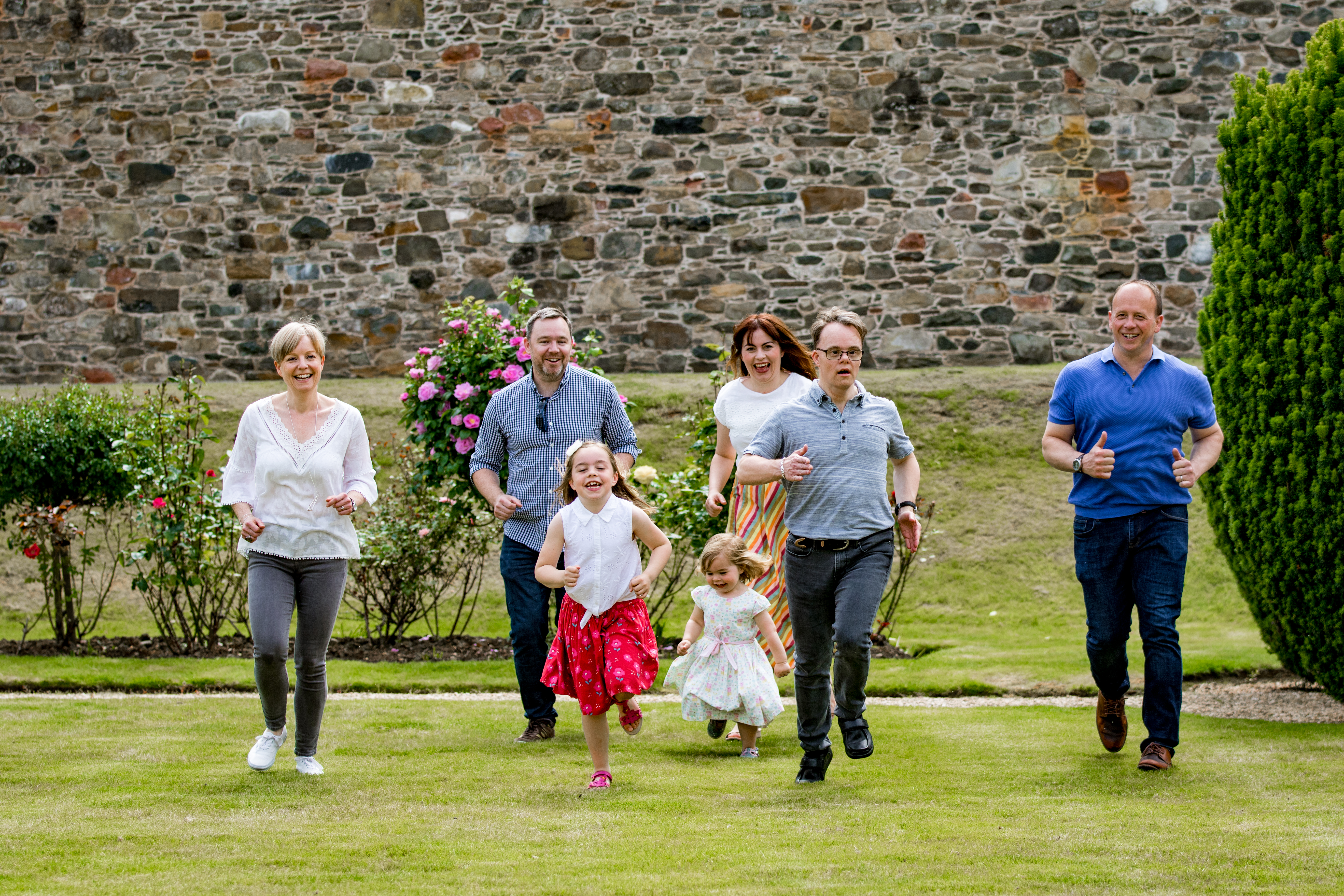 Whole family running together and laughing across a sunny walled garden lawn