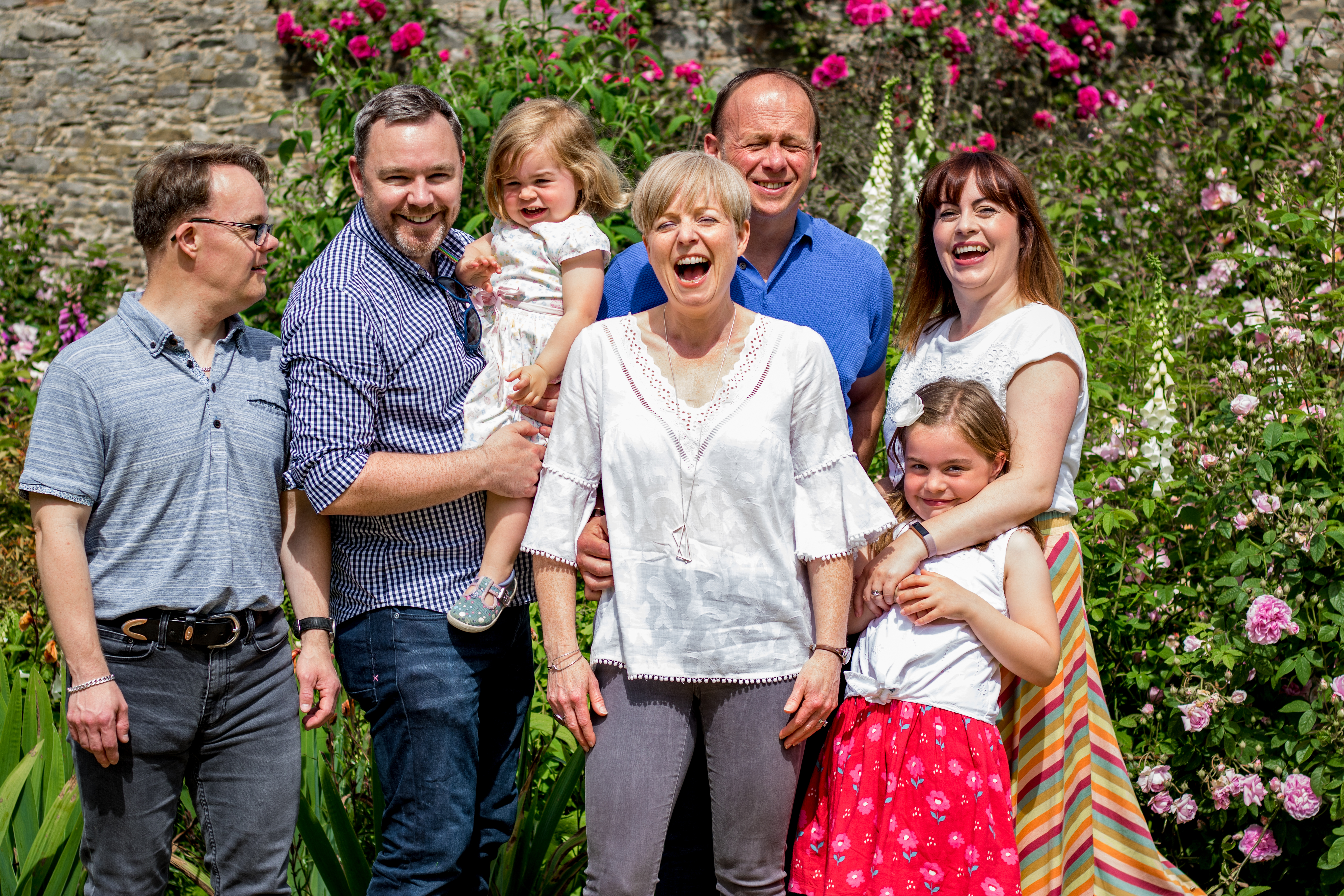 Multi-generational family laughing together among roses and foxgloves in a walled garden